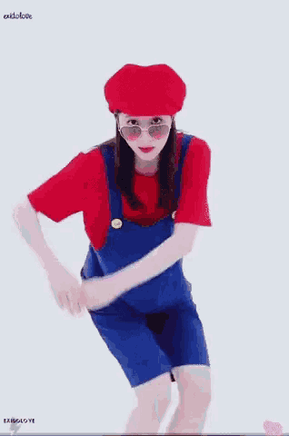 a woman in overalls and a red hat is standing in front of a white background .