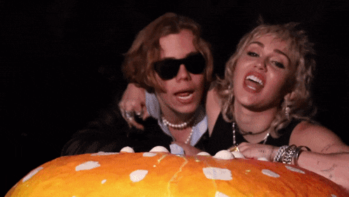 a man and a woman are posing for a picture with a pumpkin in the foreground