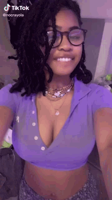 a woman wearing glasses and a purple crop top is taking a picture of herself .