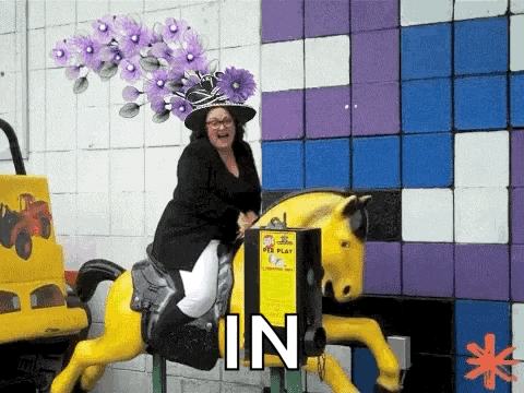 a woman wearing a purple hat is riding a carousel horse .
