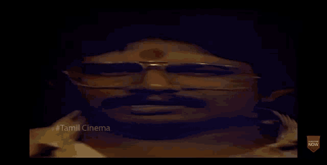 a man with glasses and a mustache is laying on a bed with his hands on his head .