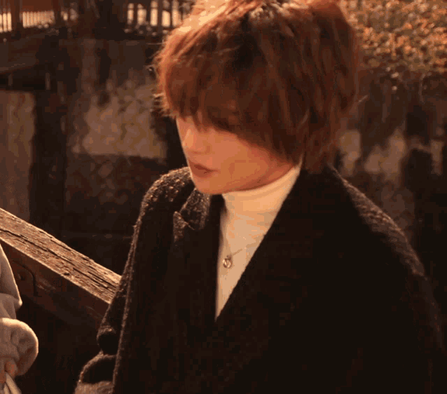 a woman wearing a black coat and a white turtleneck is looking down