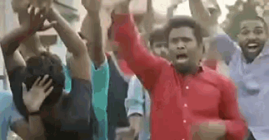 a man in a red shirt is standing in front of a crowd of people raising their hands in the air .