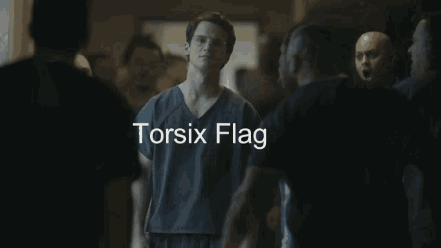 a man in a scrub top stands in a crowd with the words " torsix flag " below him