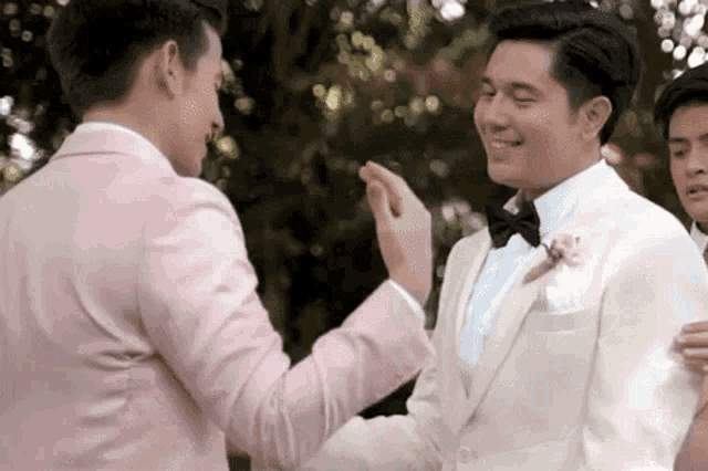two men in suits are shaking hands at a wedding reception .