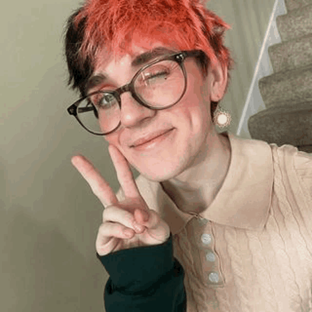 a young man wearing glasses and earrings is giving a peace sign .