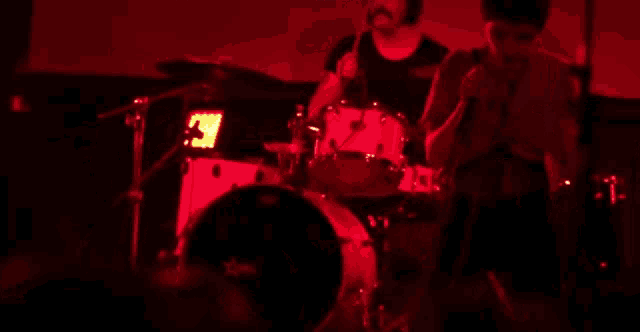 a man is playing drums in a dark room with red lights behind him