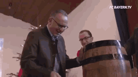 a man in a suit is pouring beer into a wooden barrel