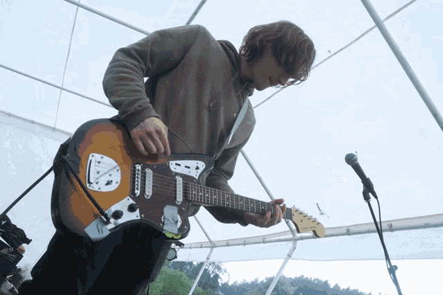 a man playing a guitar in front of a microphone that says fender
