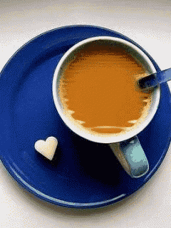 a cup of coffee sits on a blue plate next to a heart shaped sugar cube