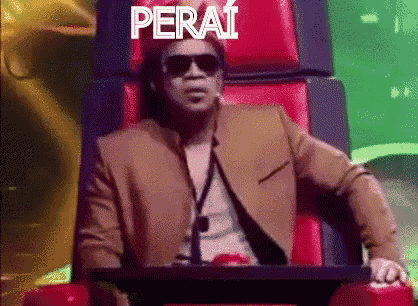 a man in a suit and sunglasses is sitting in a chair with the word perai written on it .