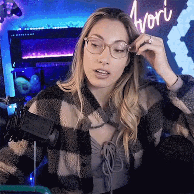 a woman wearing glasses and a plaid jacket is sitting in front of a microphone in a room .