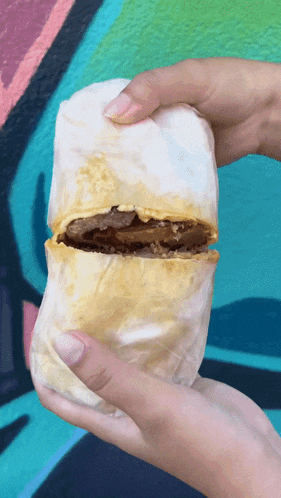 a person is holding a burrito in front of a colorful background