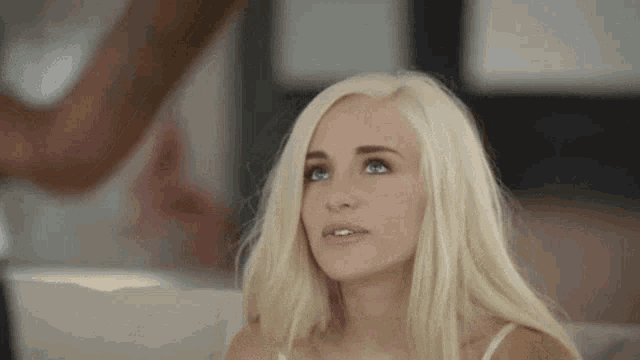 a woman with blonde hair and blue eyes is sitting on a couch and looking up .