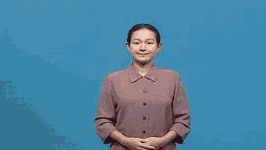a woman is wearing a purple shirt and making a sign language gesture .