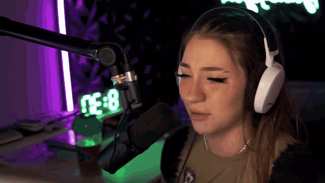 a woman wearing headphones stands in front of a microphone with a neon sign behind her that says 0:38