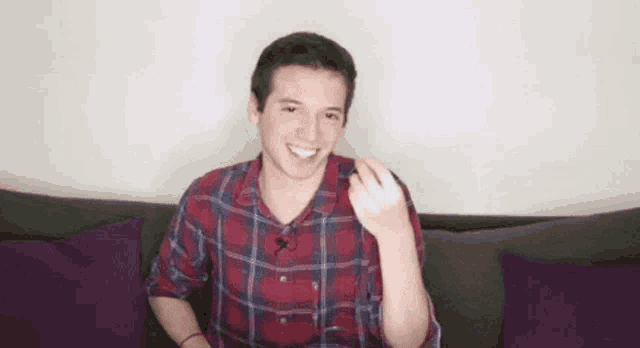 a young man in a plaid shirt is sitting on a couch with his hand out .
