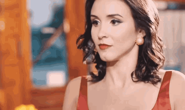 a woman in a red dress is standing in front of a window and looking at the camera .