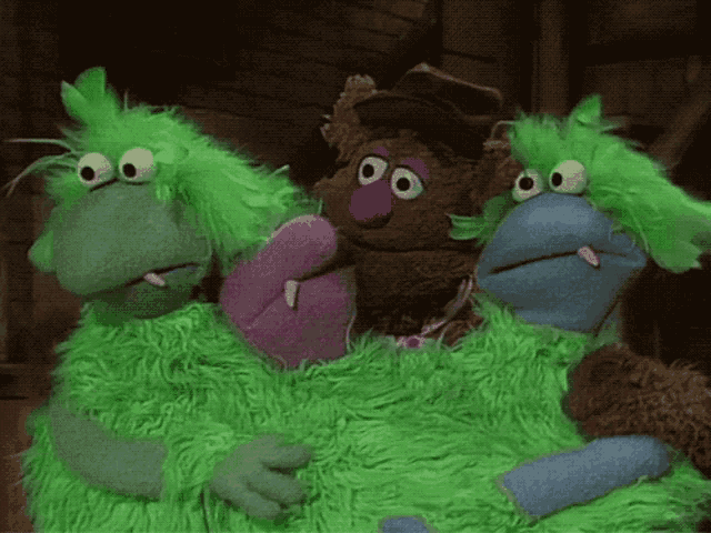 a group of green and purple stuffed animals with big eyes