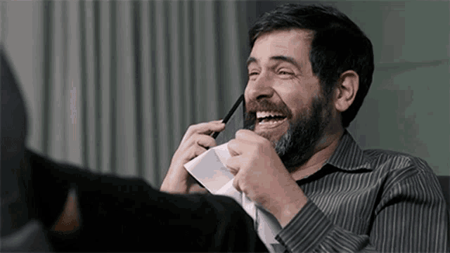 a man with a beard laughs while talking on a cell phone