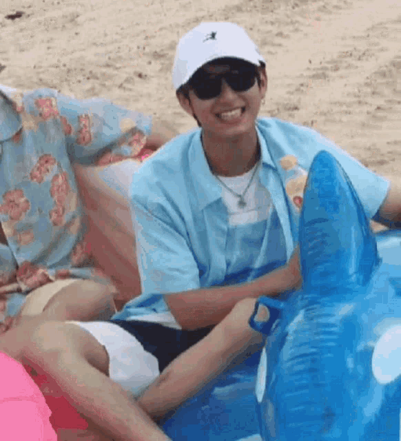 a man wearing sunglasses and a white hat is sitting on an inflatable whale on the beach