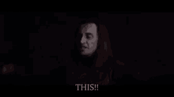 a man with long hair says " this " in a dark room