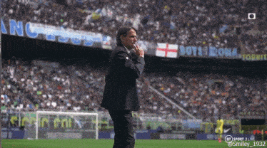 a man in a suit stands on a soccer field in front of a banner that says boys