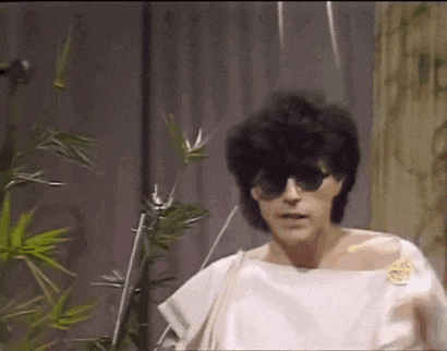 a woman wearing sunglasses and a white top is standing next to a plant .
