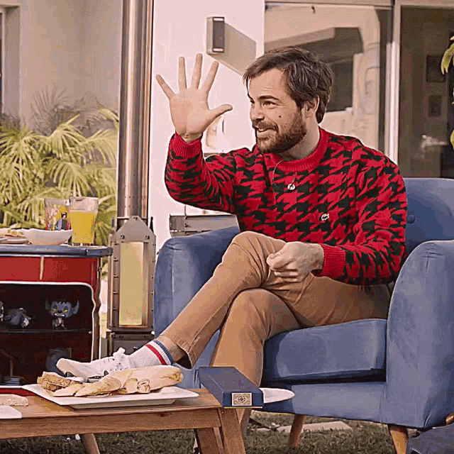 a man in a red and black sweater sits in a chair with his legs crossed