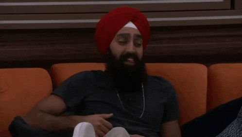 a man with a beard is sitting on a couch wearing a red turban .