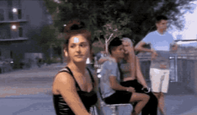 a woman in a black tank top is sitting in a chair with other people