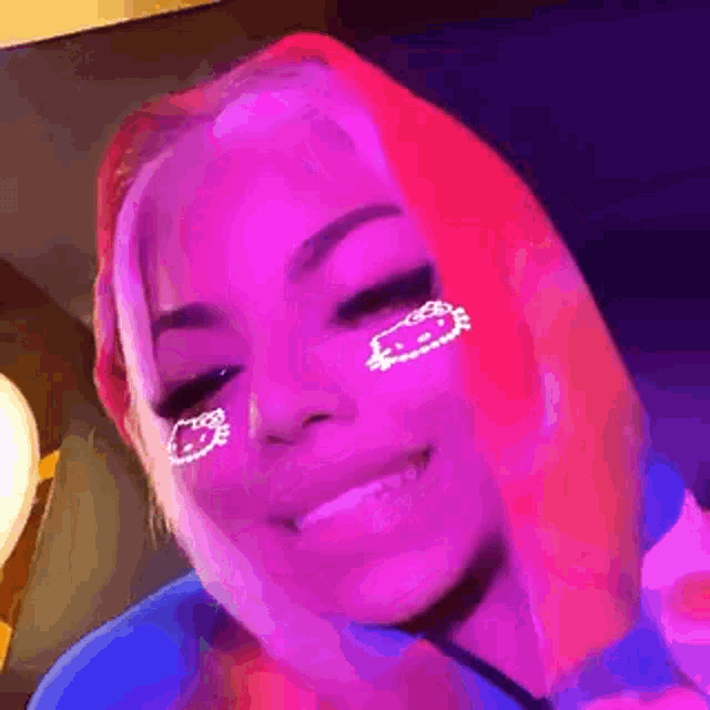 a woman with pink hair and a hello kitty face paint on her face is smiling .