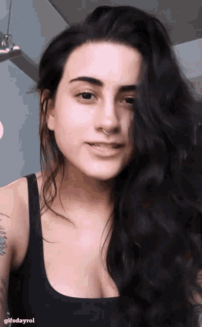 a woman with long black hair and a nose ring looks at the camera with gifsdayrol written below her