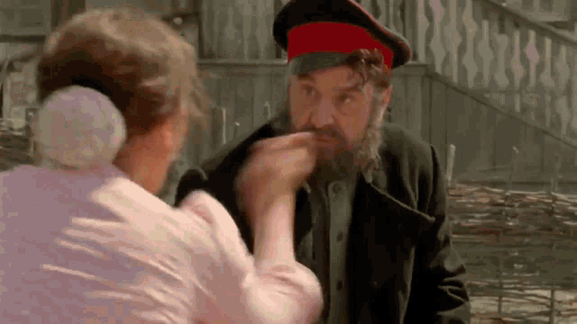 a man with a beard and a red hat is talking to a woman