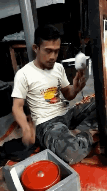 a man wearing a white shirt that says ' hawaii ' on it sits on the floor