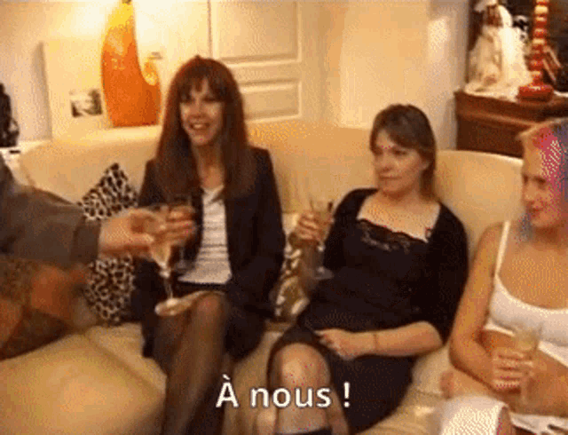 a group of women are sitting on a couch with a man toasting them with champagne