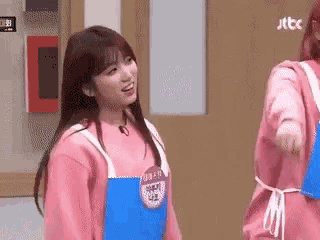 a girl in a pink sweatshirt and blue apron is standing next to another girl in a pink sweatshirt and blue apron .