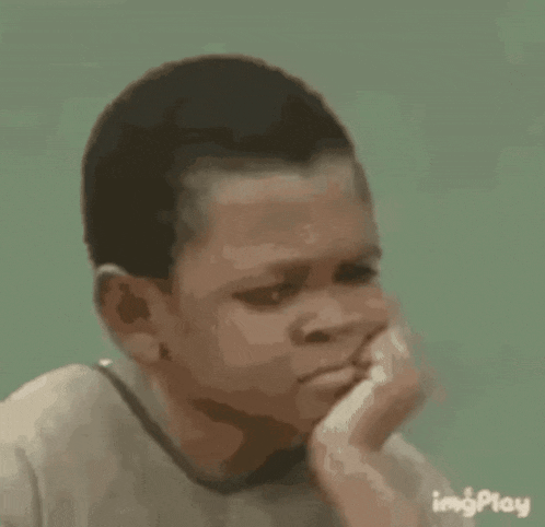 a young boy is sitting down with his hand on his chin .