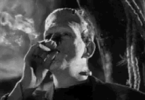 a black and white photo of frankenstein smoking a cigarette in a forest .