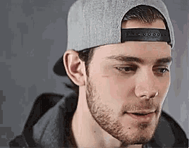 a man with a beard wearing a baseball cap and a black jacket