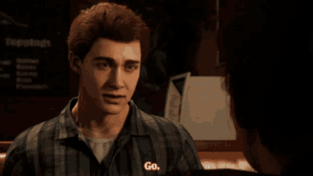 a man in a plaid shirt is talking to another man in a dark room and says go