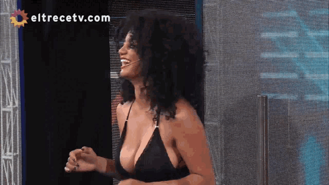 a woman in a black bikini is laughing in front of a screen that says eltrecetv.com