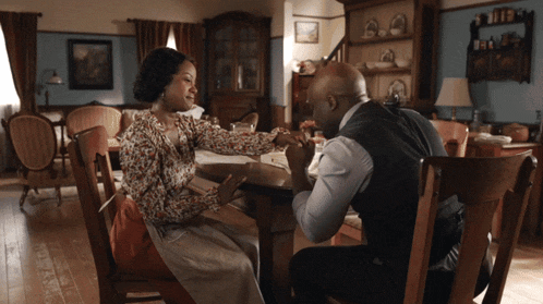 a man and a woman sitting at a table holding hands