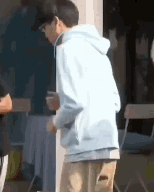 a man in a light blue hoodie is standing in front of a window .