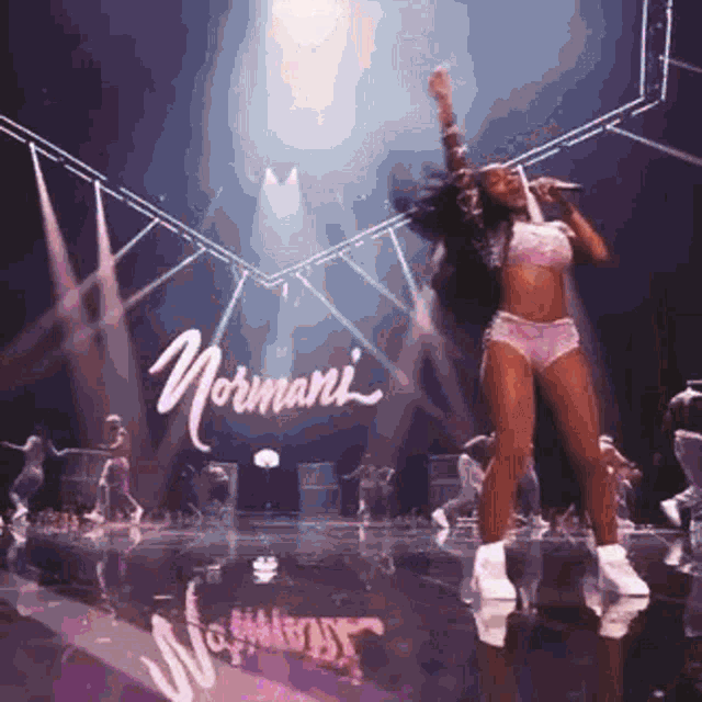 a woman is singing into a microphone while dancing on a stage in front of a sign that says normani .