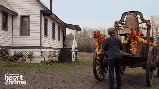 a man stands in front of a horse drawn carriage decorated with leaves and a bell on the back