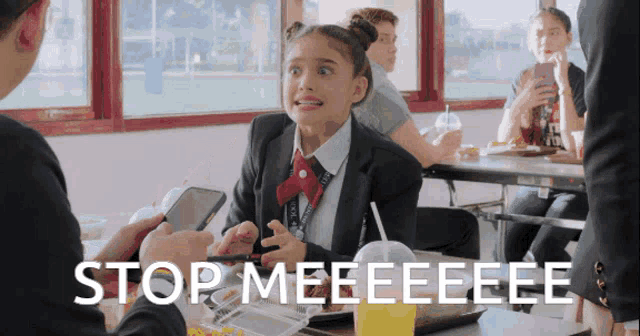 a girl in a school uniform is sitting at a table with the words stop meeeeeeee written on the screen