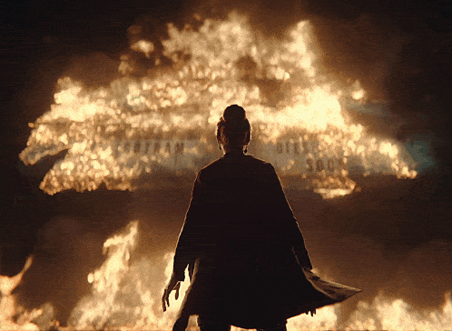 a woman stands in front of a large fire and a sign that says gotham city soon
