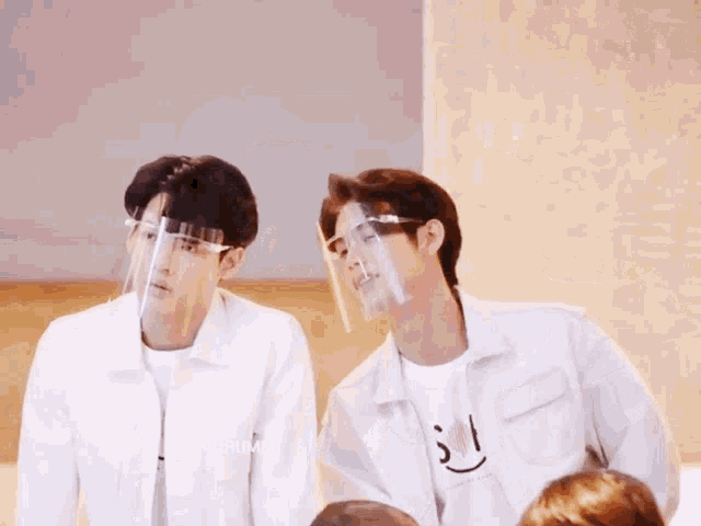 two men wearing face shields are standing next to each other in a room