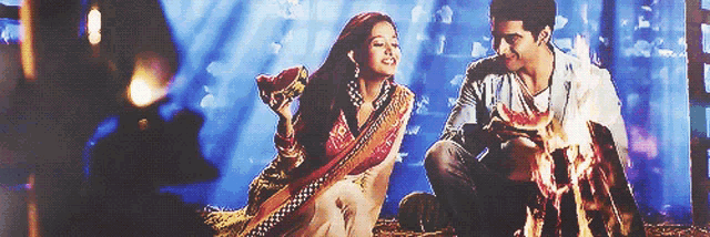 a man and a woman sitting next to a fire